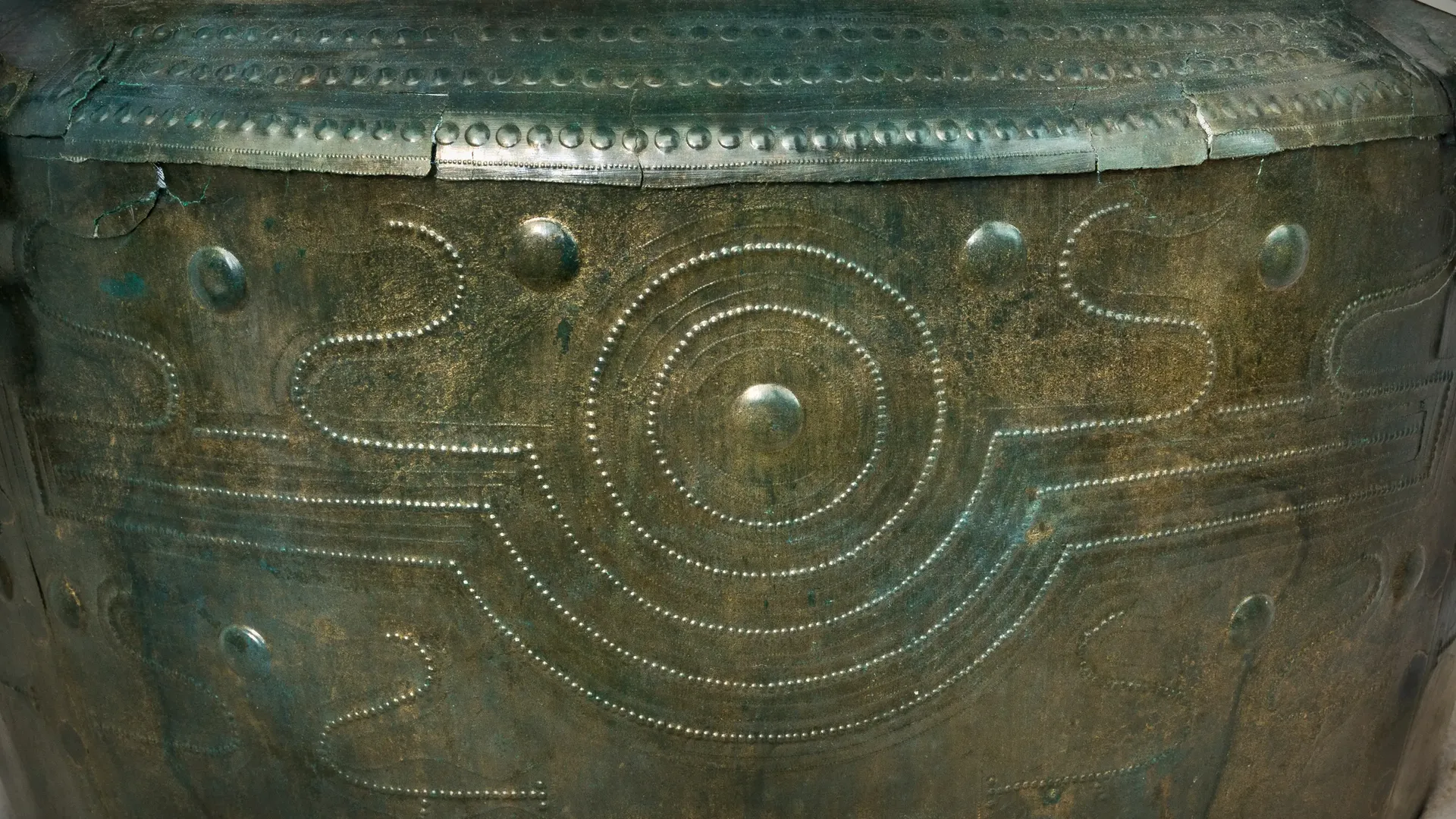 Detailaufnahme: Muster aus Kreisen umgeben von Wasservögeln und Buckelreihen aus großen und kleinen Buckeln auf grünem Bronzeblech.