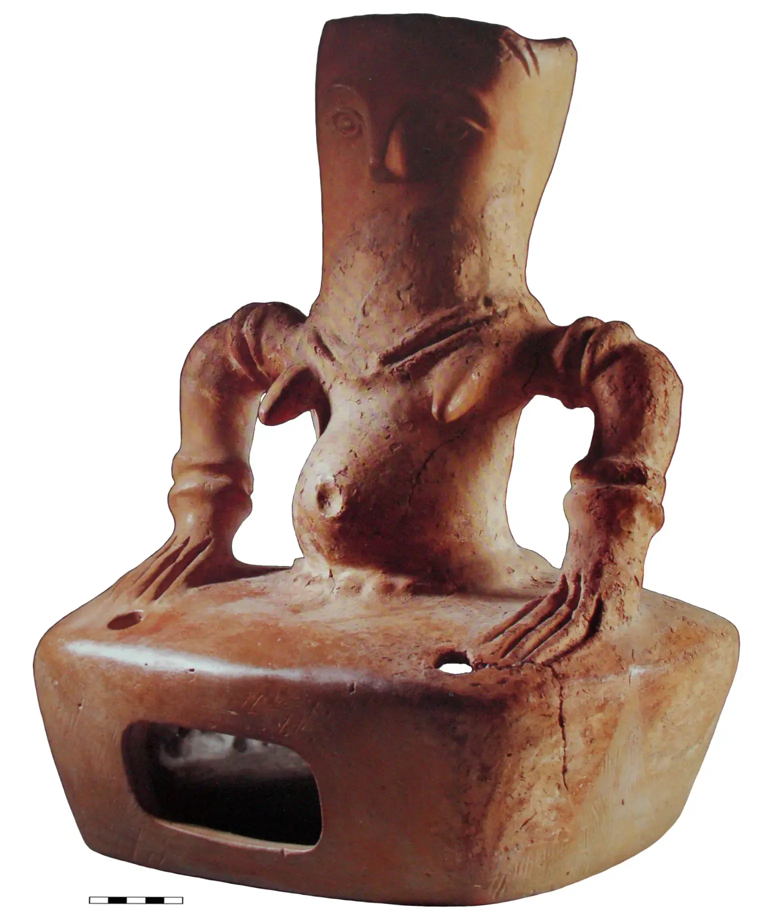 Abstrahierte Figur in menschlicher Form aus hellbrauner Keramik mit Ergänzungen. Der Kopf ist flach. Nase, Augen, Brüste, ein runder Bauch und Schmuck an Hals und Armen sind betont. Hüftabwärts ein Quader, auf den sie die Hände stützt.