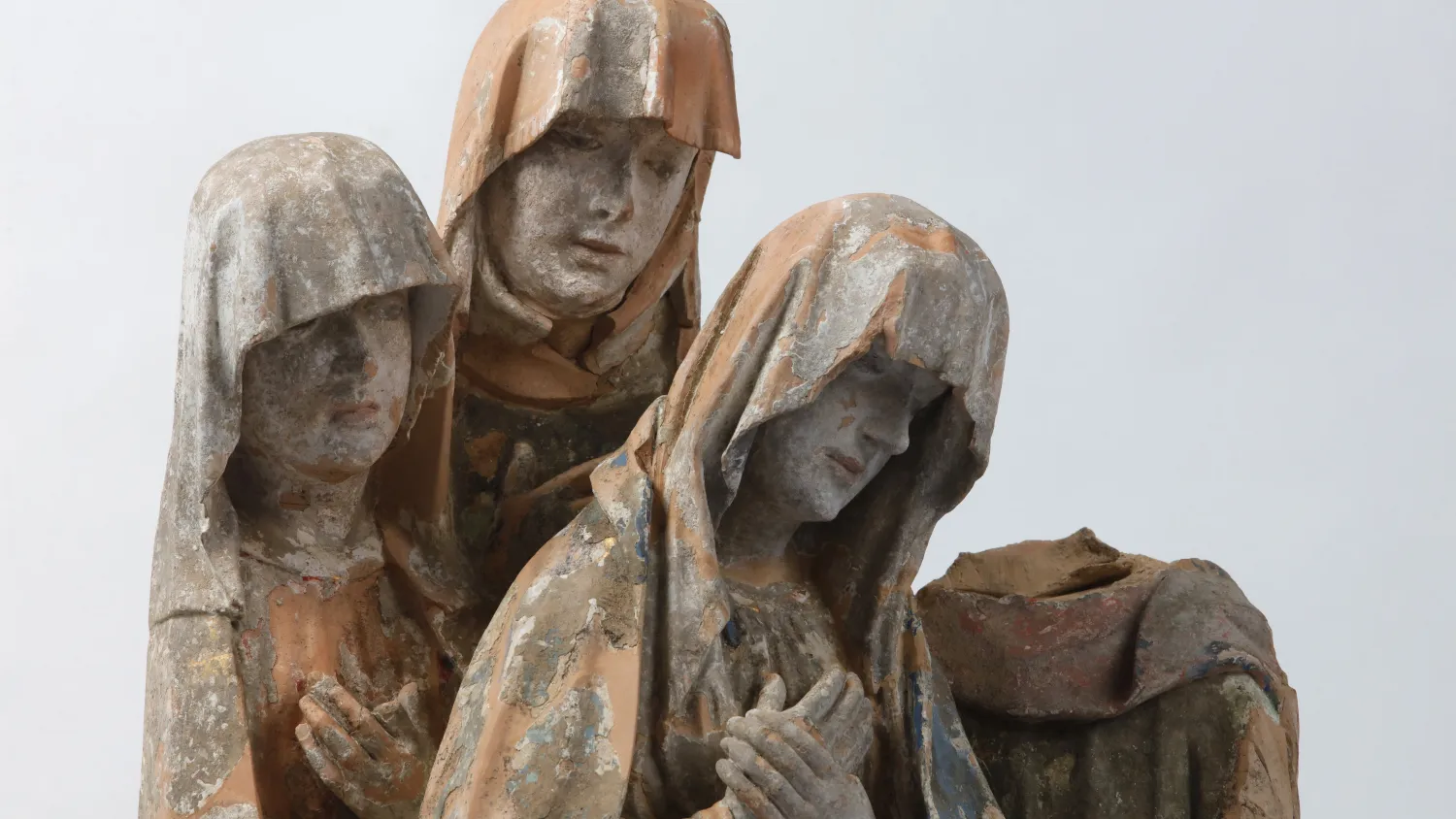 Detail einer Statuengruppe aus vier Figuren mit Resten von bunter Bemalung. Drei Figuren blicken nach unten und kreuzen die Hände vor der Brust. Sie tragen Schleier. Der vierten Figur fehlt der Kopf.