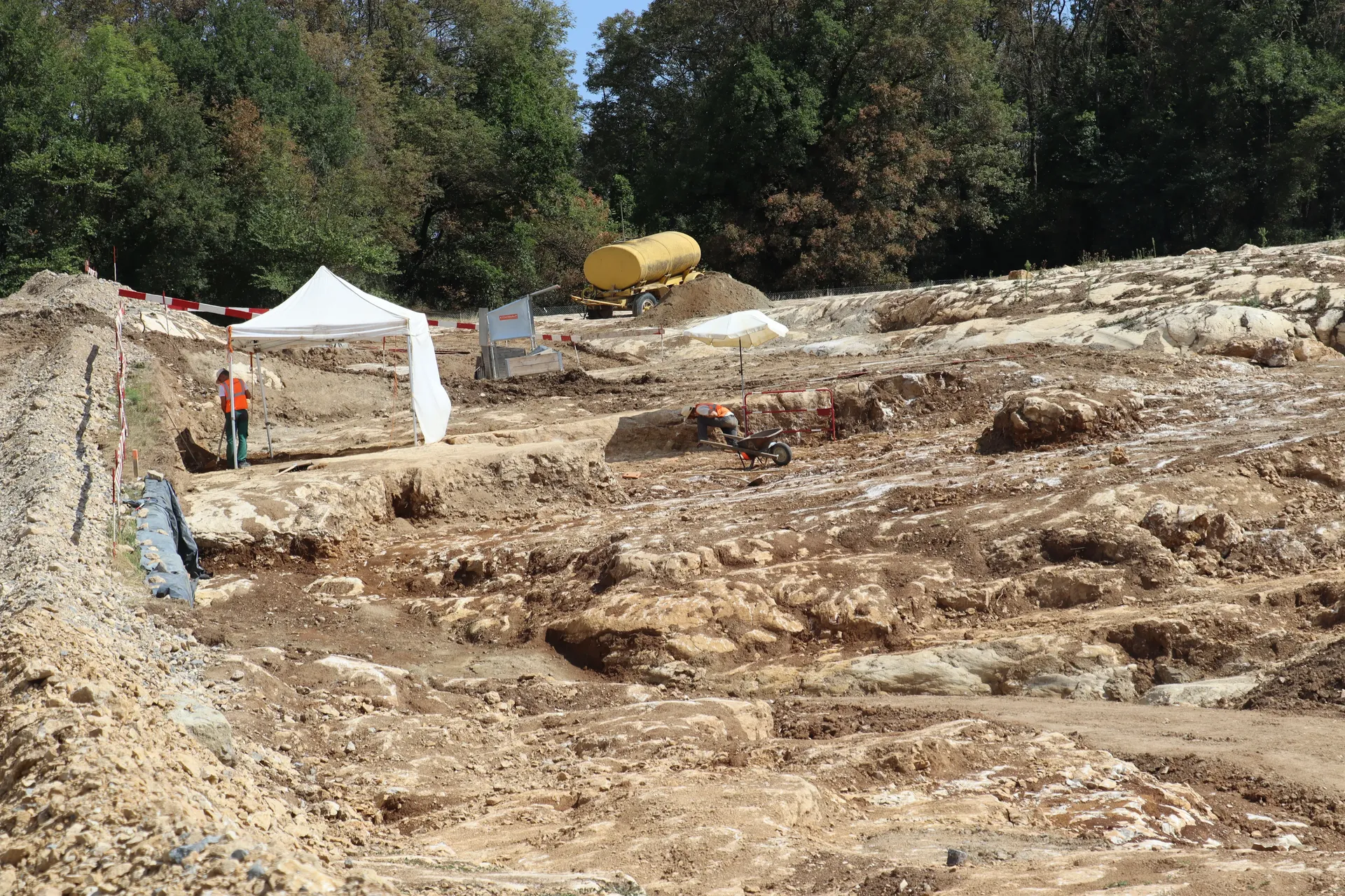 Fläche einer archäologischen Ausgrabung auf einem felsigen Untergrund. Im Hintergrund arbeiten zwei Personen.