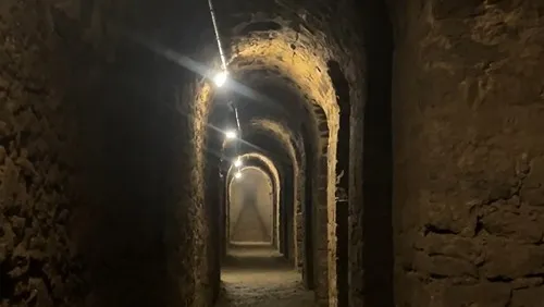 Ein dunkler, enger und gewölbter Gang aus gemauertem Stein. Er ist nur schummrig beleuchtet.