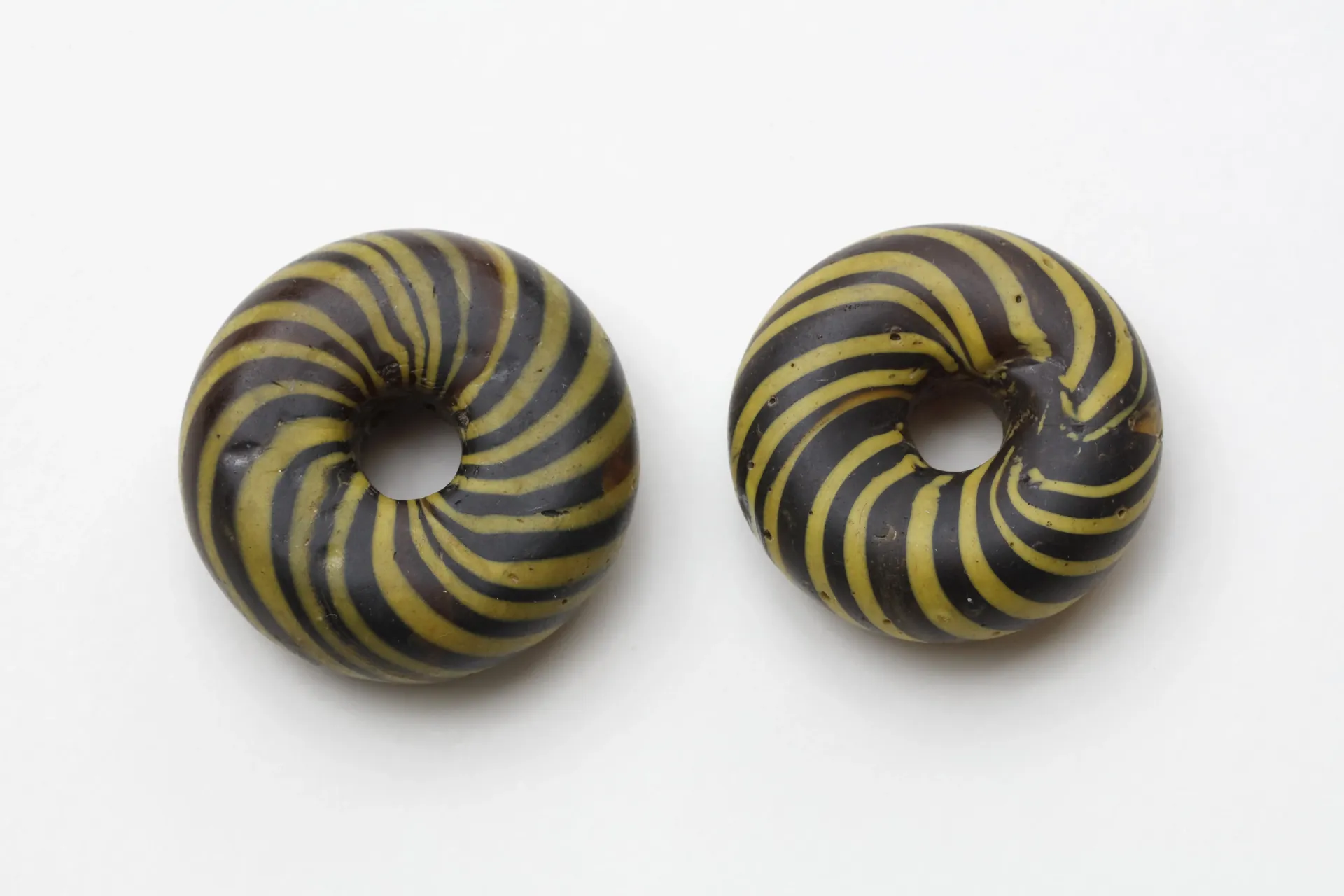 Zwei runde, flache und gelb-schwarz gestreifte Glasperlen.
